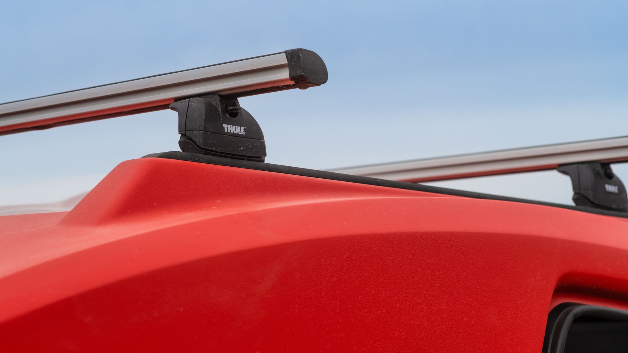 Detail of Thule roof rack crossbars mounted to the red Escapod TOPO2 MTB trailer, set against a light blue sky.