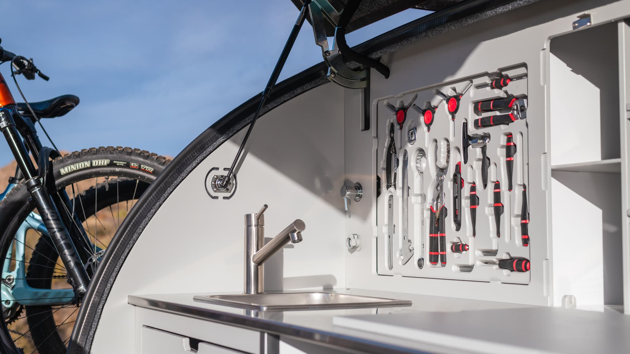 Open galley of the TOPO2 MTB with Feedback tools and a bike visible behind it, showcasing the trailer’s integrated workspace and sink.