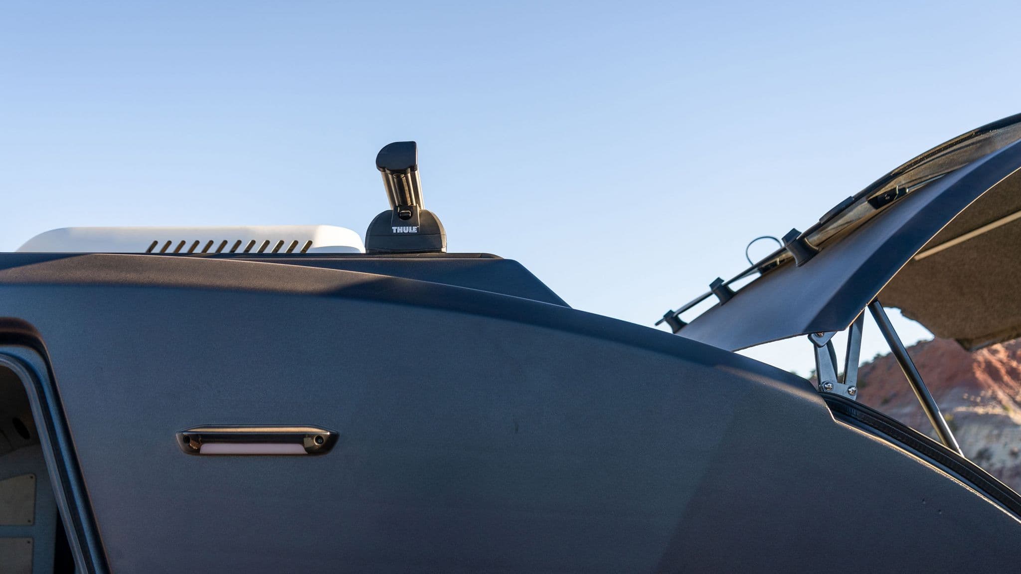 Side profile of an Escapod trailer's aerodynamic roofline, featuring a Thule roof rack system and pop-up galley hatch for storage and convenience.