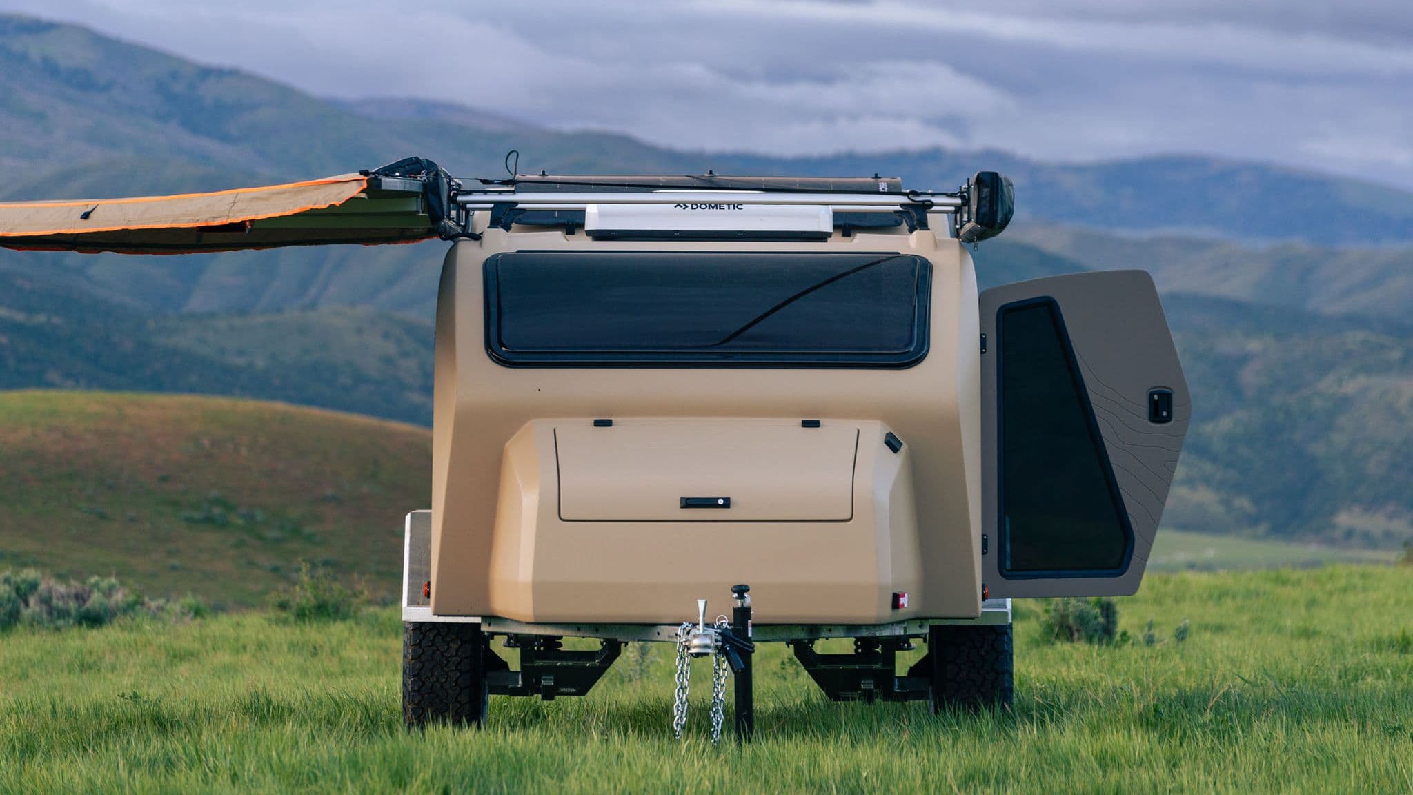 Back view of the Escapod TOPO2 trailer with the rear hatch closed and door open, revealing its durable fiberglass body against a scenic mountain backdrop.