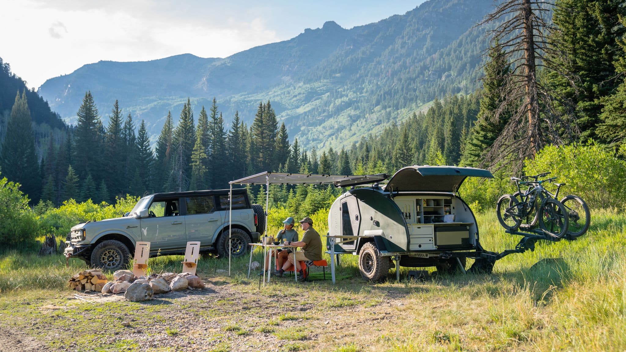 Escapod trailer and Ford Bronco set up for camping in a remote alpine valley with bikes mounted on the trailer.