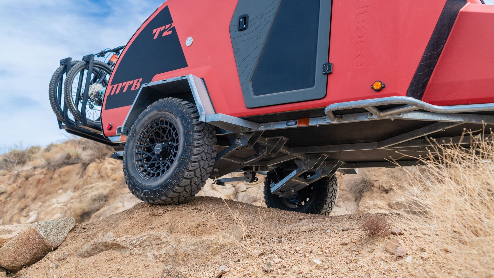 The Escapod TOPO2 in lava orange flexing over a steep rocky incline, showing off its high-clearance off-road suspension.