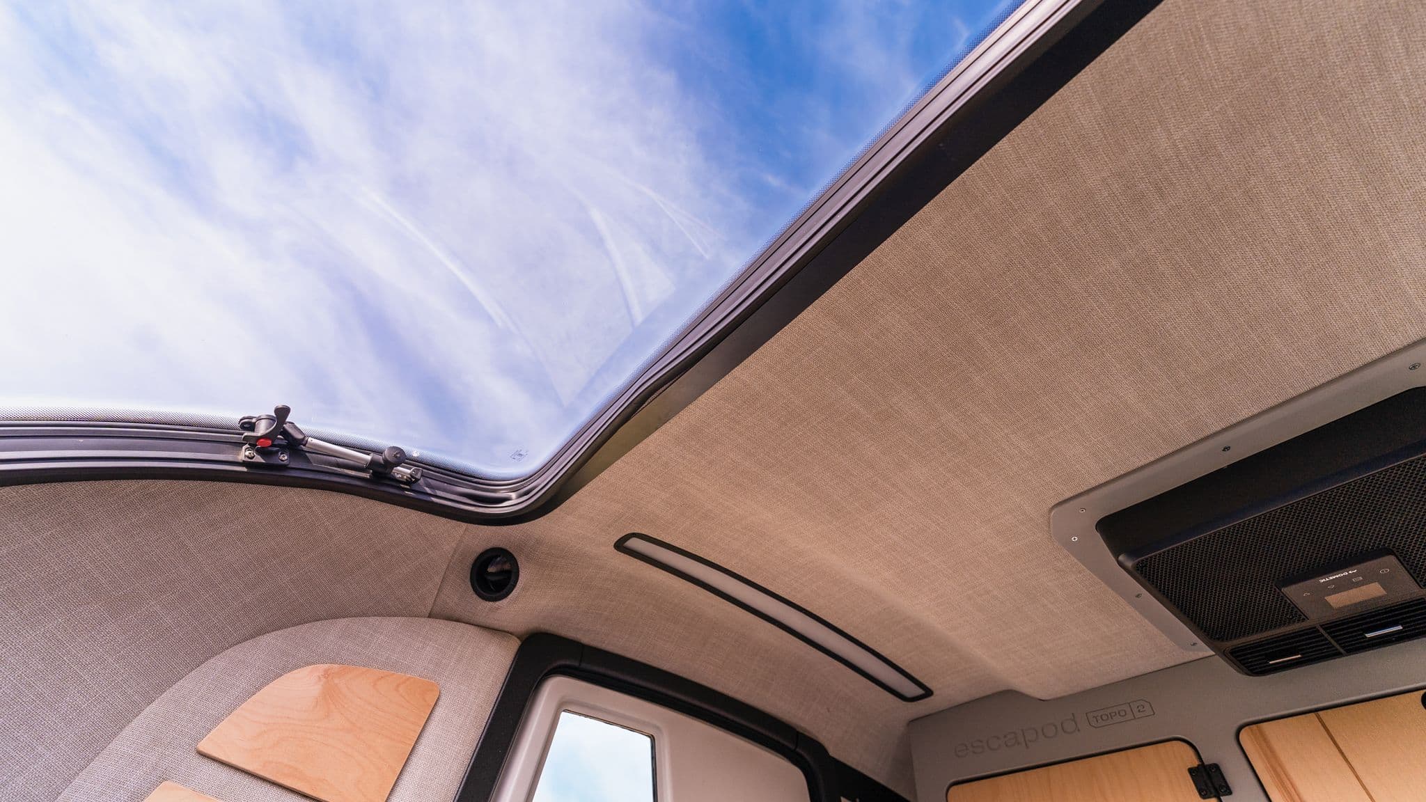 Interior shot looking up through the TOPO2’s panoramic skylight, showing blue skies and a textured beige ceiling for a cozy camping experience.