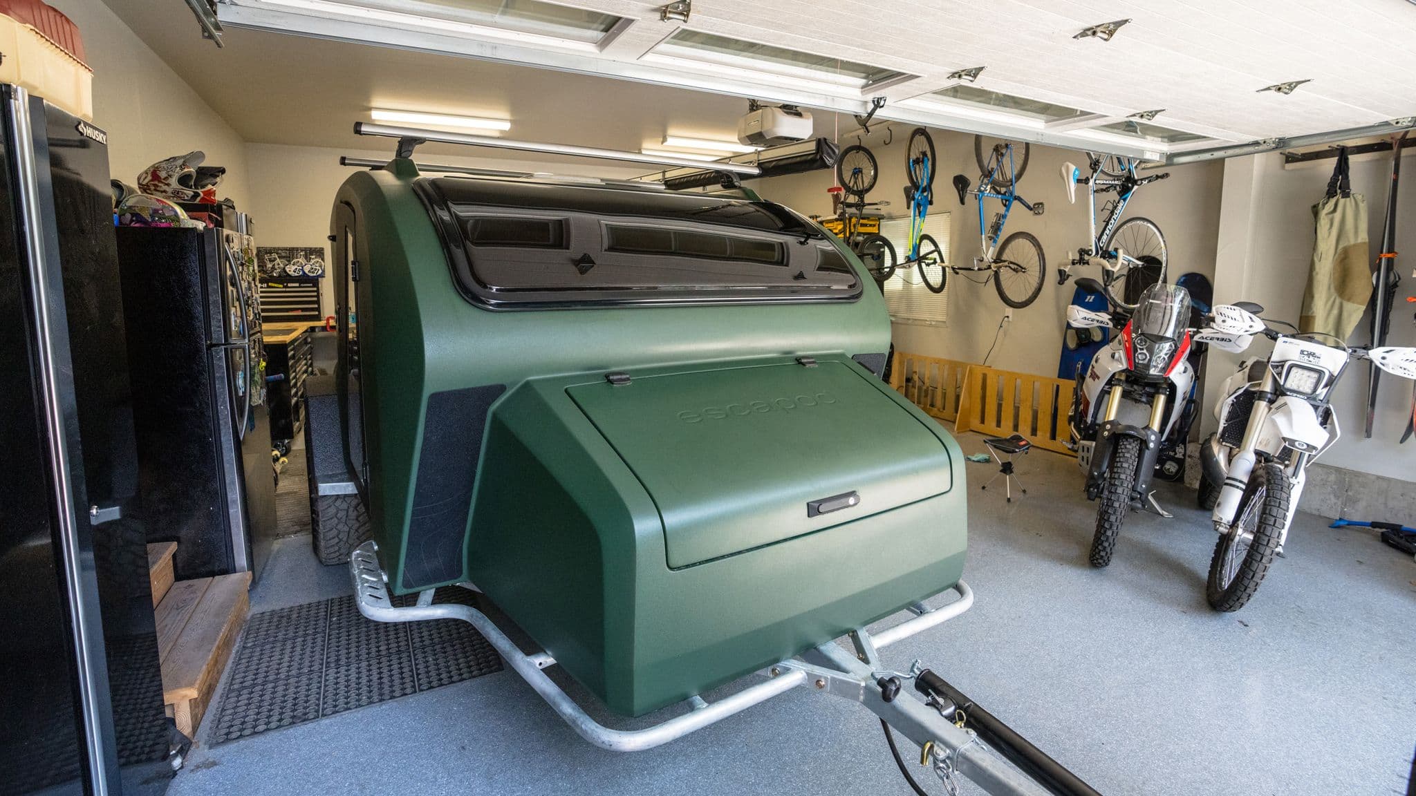 Green Escapod trailer parked in a garage alongside motorcycles and outdoor gear.