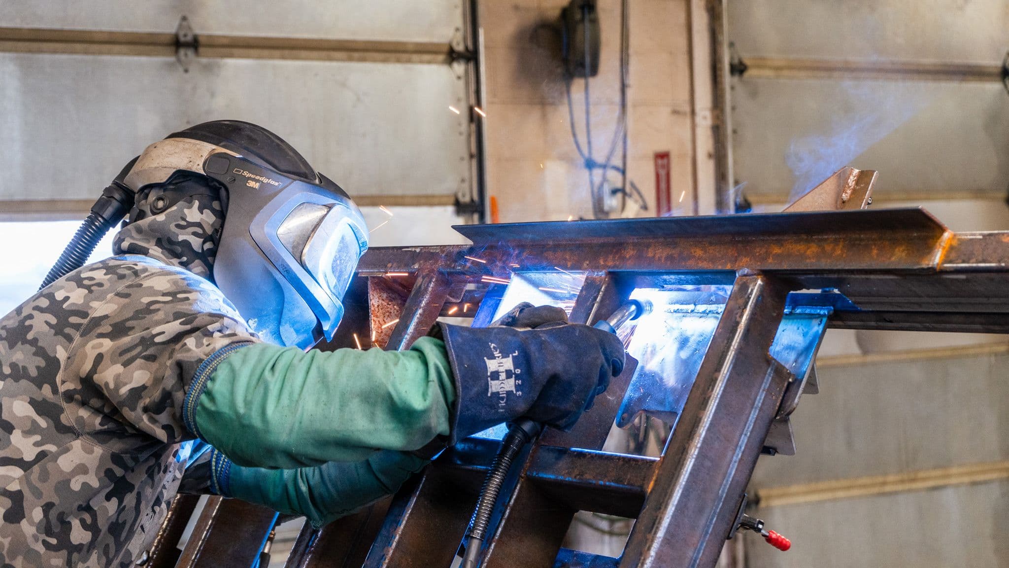 A close-up of a welder in safety gear using a welding torch to join metal pieces, with bright sparks flying inside the Escapod manufacturing facility.