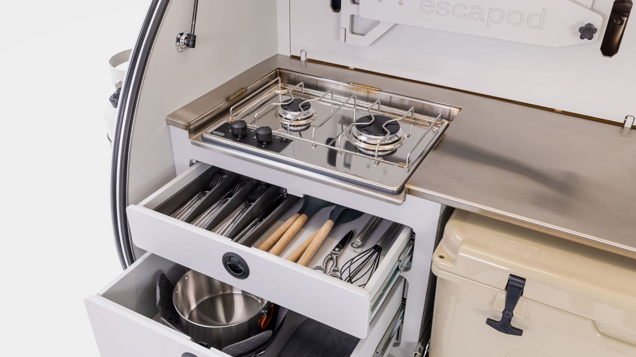 Open galley of the Escapod TOPO trailer, showing a well-organized kitchen with a two-burner gas stove, storage drawers, and a YETI cooler.