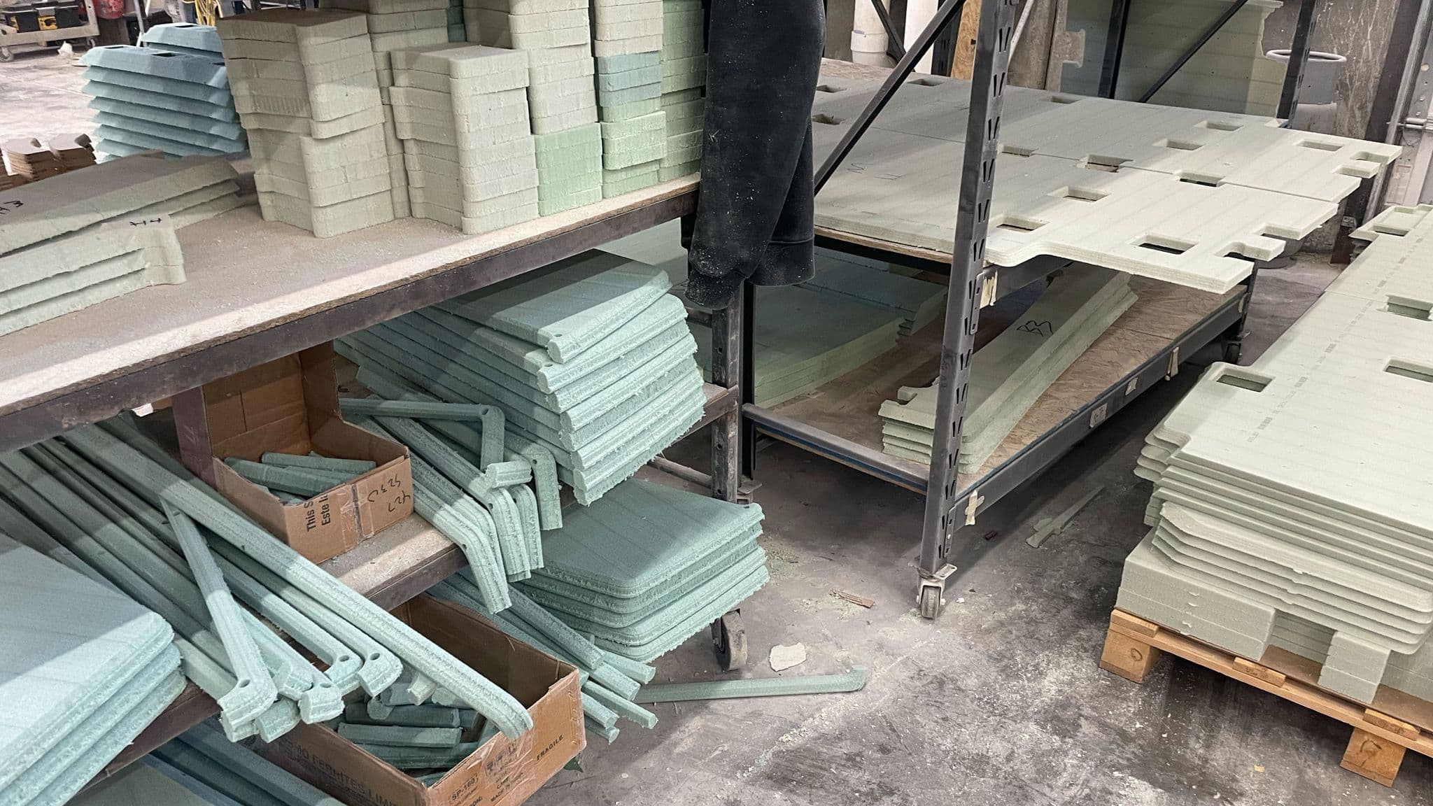 Stacks of low-density PET foam core cutouts and shaped pieces on metal shelving inside the Escapod factory, used for insulation and structural support in fiberglass trailers.