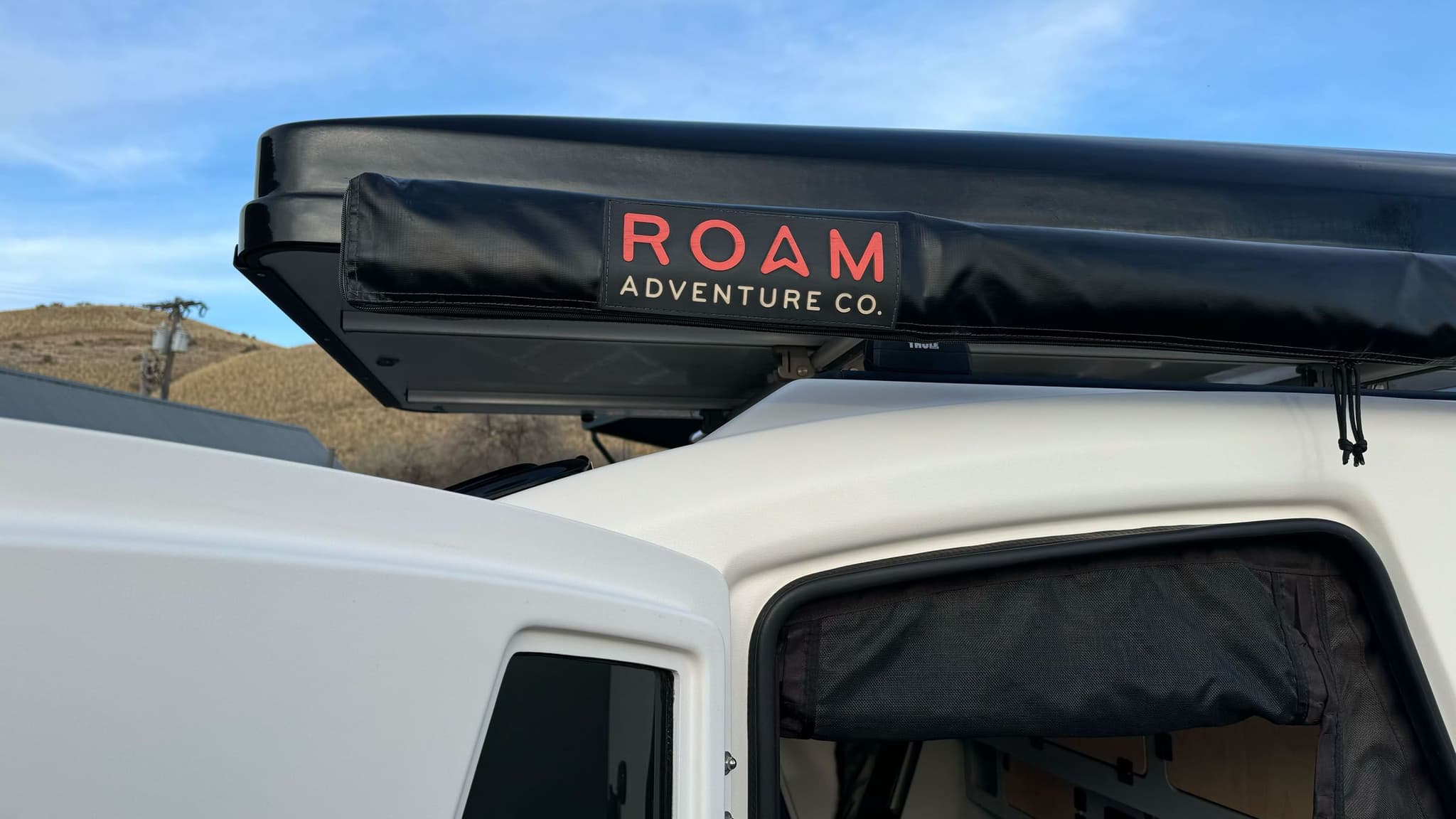 Exterior of a white 2023 Escapod TOPO2, photographed at Escapod's headquarters in Coalville, UT, with a ROAM awning and an iKamper Tent.