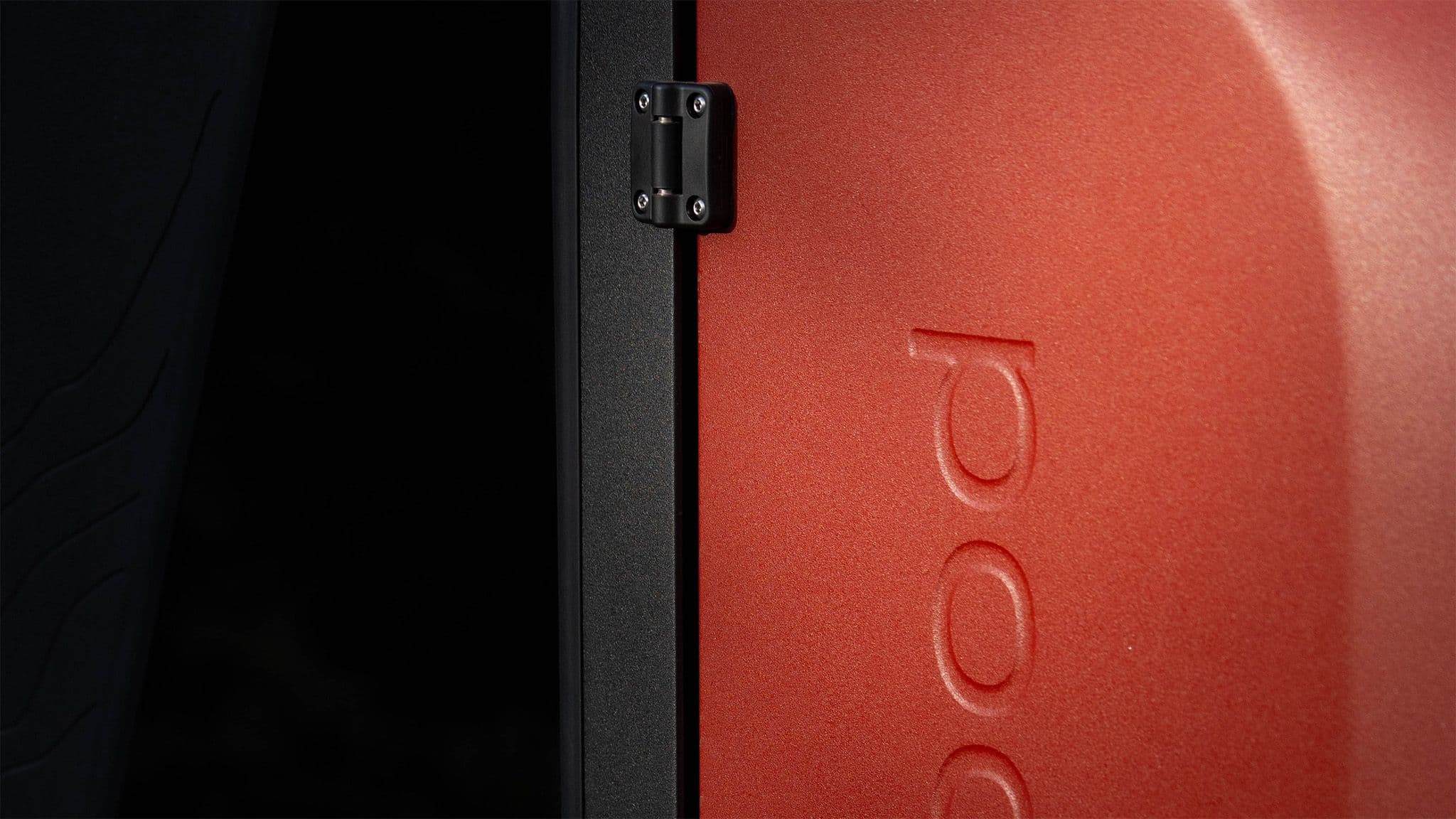 Close-up of a red Escapod trailer door with embossed branding, black window frame, and a rugged matte finish.