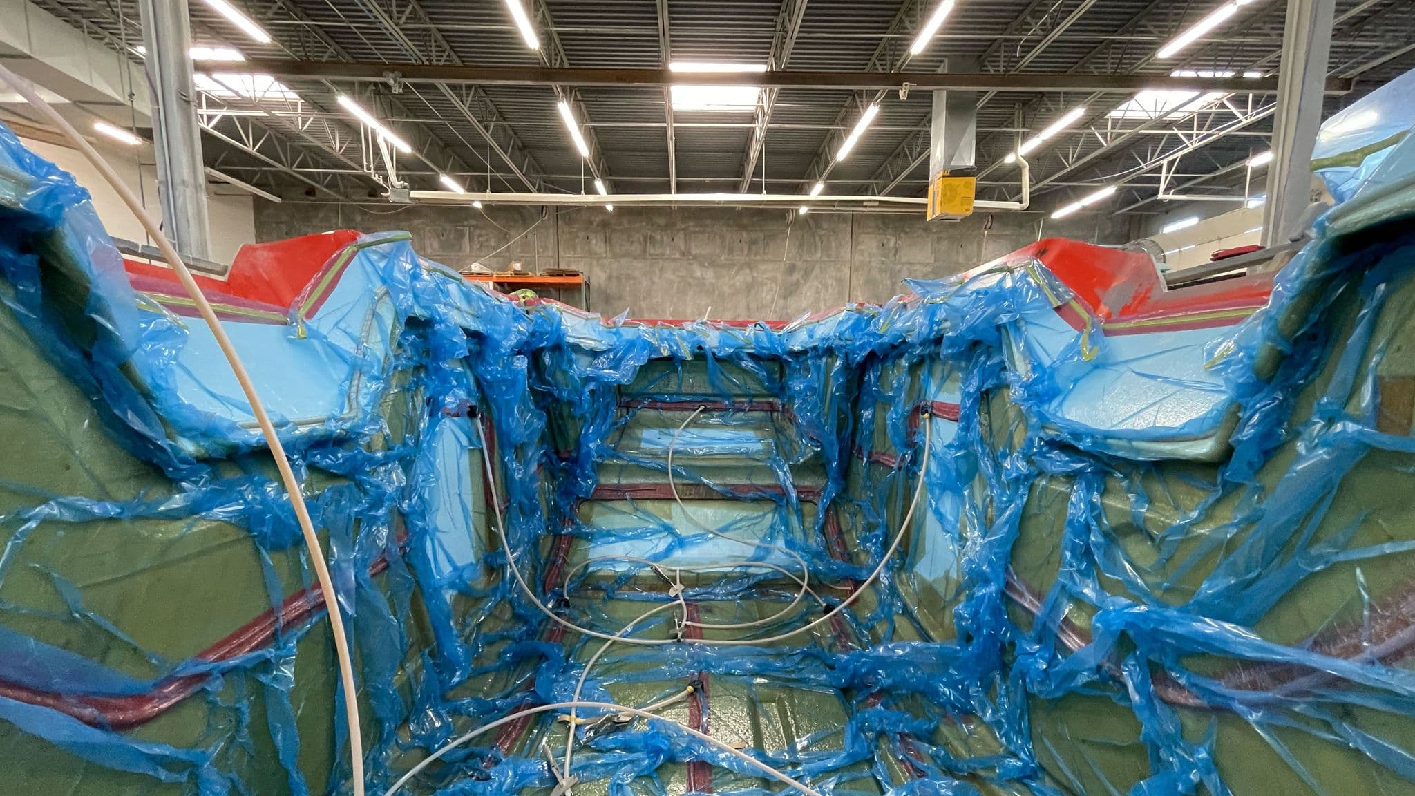 Interior of the Escapod production facility showing the fiberglass vacuum bag infusion process with blue plastic sheeting over a mold.