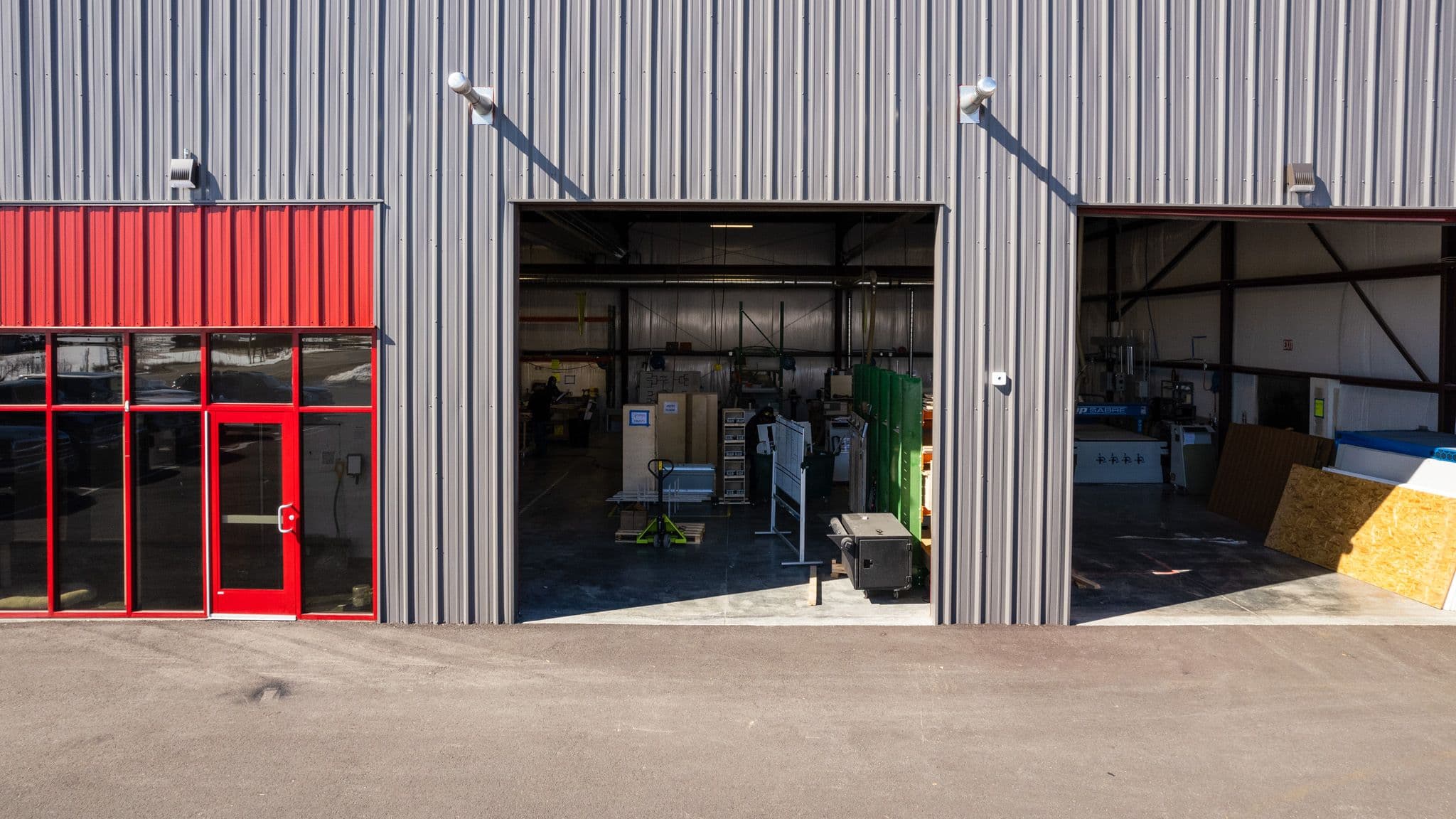 Close-up view of the Escapod factory entrance with red doors and an open garage bay, revealing the interior of the workshop.
