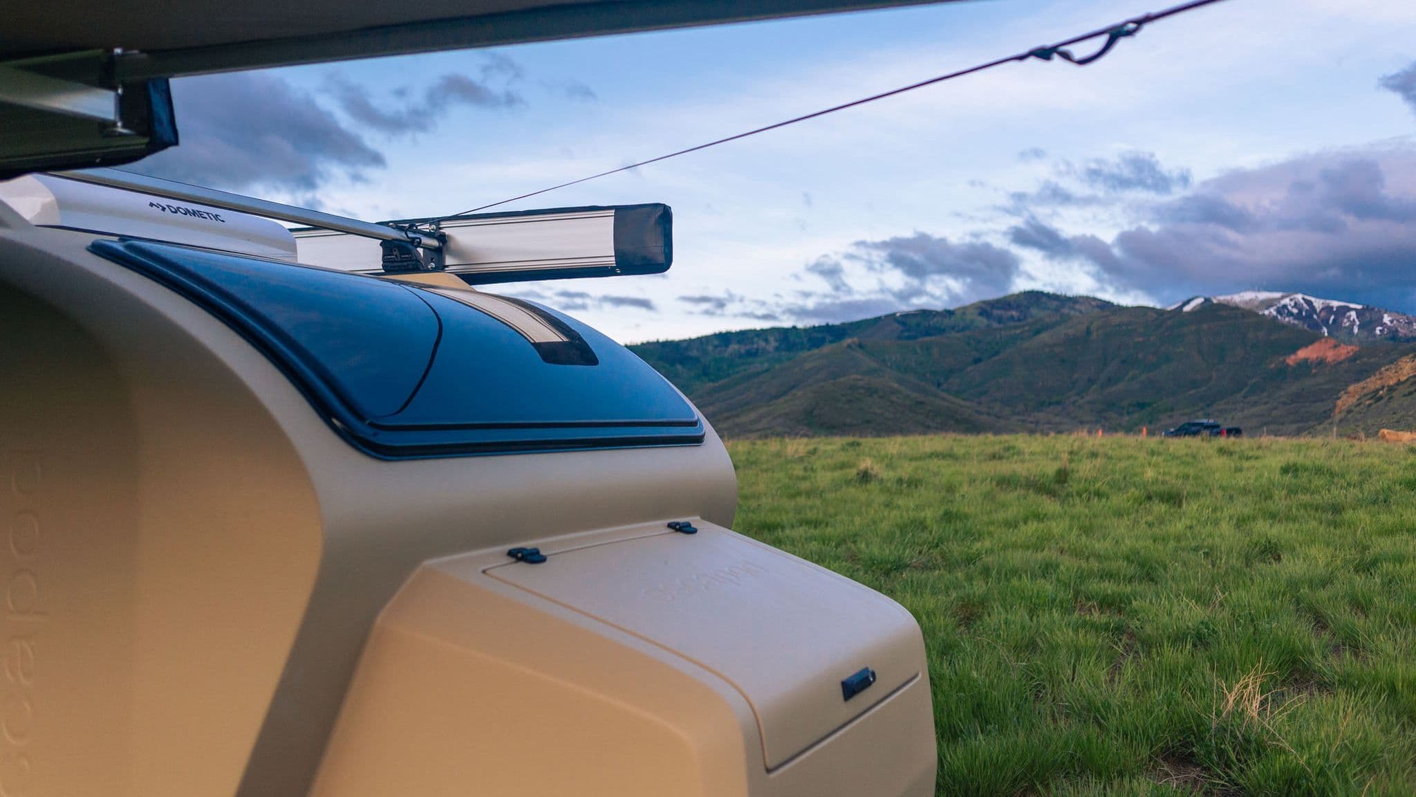 Close-up of the Escapod TOPO2 front storage compartment and large panoramic window, overlooking vast green hills and a snow-capped mountain range.