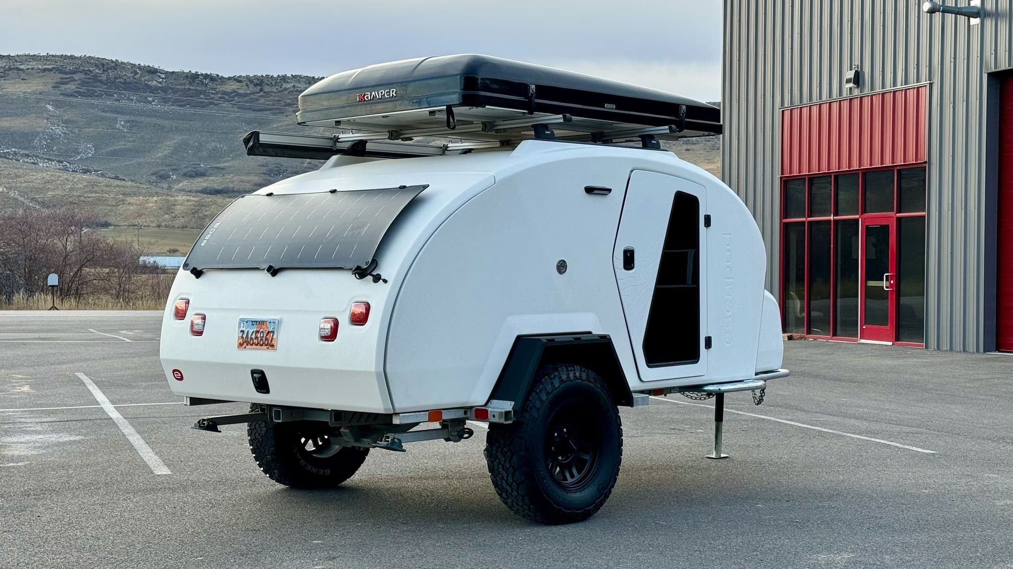 Exterior of a white 2023 Escapod TOPO2, photographed at Escapod's headquarters in Coalville, UT, with a ROAM awning and an iKamper Tent.